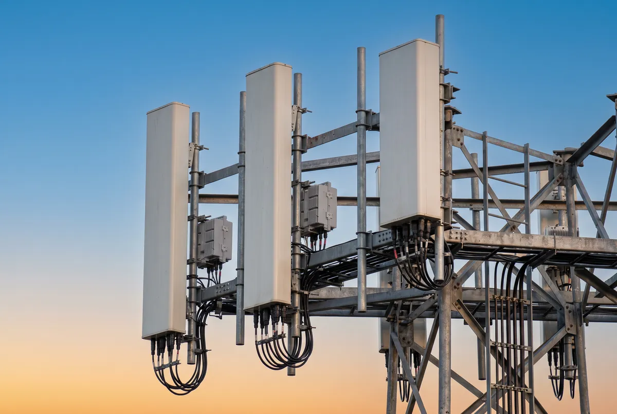 Close-up of white 5G panel antennas and remote radio units mounted on a tower sector frame at sunset